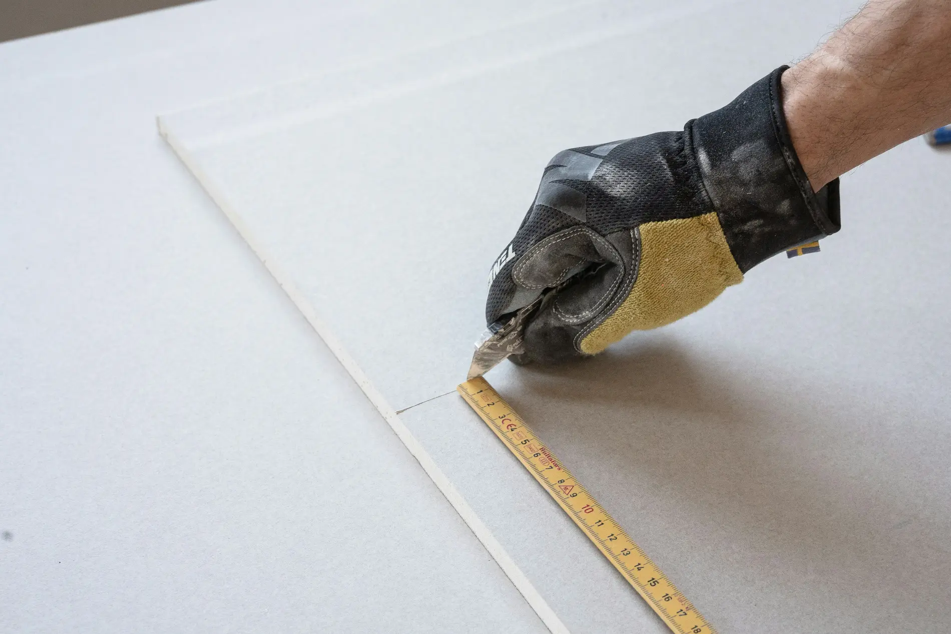 Main gantée coupant une plaque de plâtre tout en mesurant avec un mètre ruban